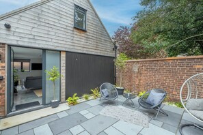 A modern house with a large sliding glass door leading to a living area, a brick wall, and a patio with outdoor furniture.
