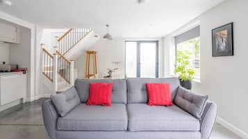 Un salon moderne avec un canapé gris, des coussins rouges, un escalier et une grande fenêtre.