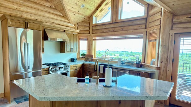 Een houten cabin interieur met een groot keukeneiland, inbouwapparatuur en een vloer van stenen tegels.
