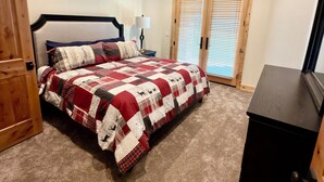 Een slaapkamer met een bed, een dressoir, een nachtkastje, een lamp en een raam met jaloezieën.