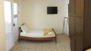 A single bed with a mattress, pillows, and a blanket in a room with a tiled floor, a wardrobe, and a television on the wall. - Triple room with it's own bathroom and balcony. (Budva)