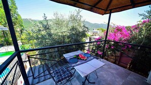 A balcony with a table set for two, overlooking a mountainous landscape with greenery and pink flowers.