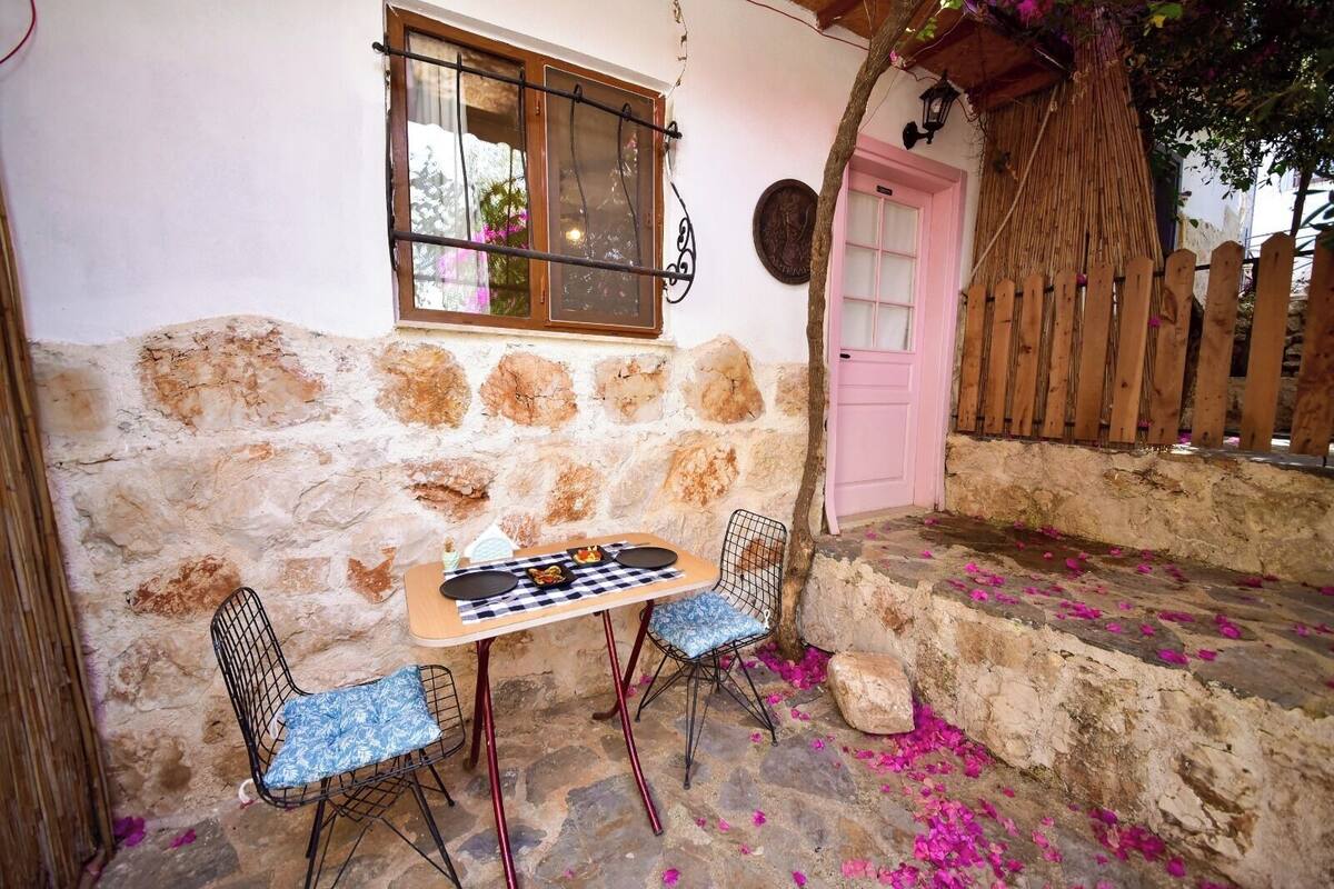 A stone wall with a window, a pink door, and a table with chairs.