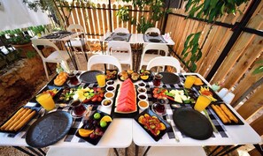 Un espacio de comedor al aire libre con varias mesas dispuestas para el desayuno, rodeado por una valla de madera y plantas en macetas.