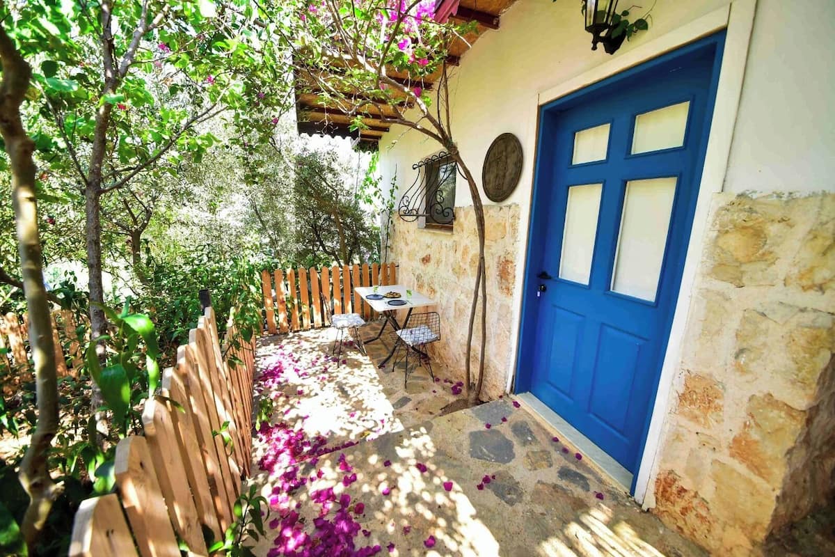A stone building with a blue door, a wooden fence, and a table with chairs outside.