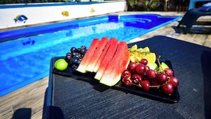 A poolside table with a fruit platter, a pool, and lounge chairs.