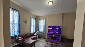 Una sala de estar con un sofá de cuero marrón, una mesa de centro, un televisor de pantalla plana y un radiador.