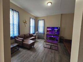 Una sala de estar con un sofá de cuero marrón, una mesa de centro, un televisor de pantalla plana y un radiador.
