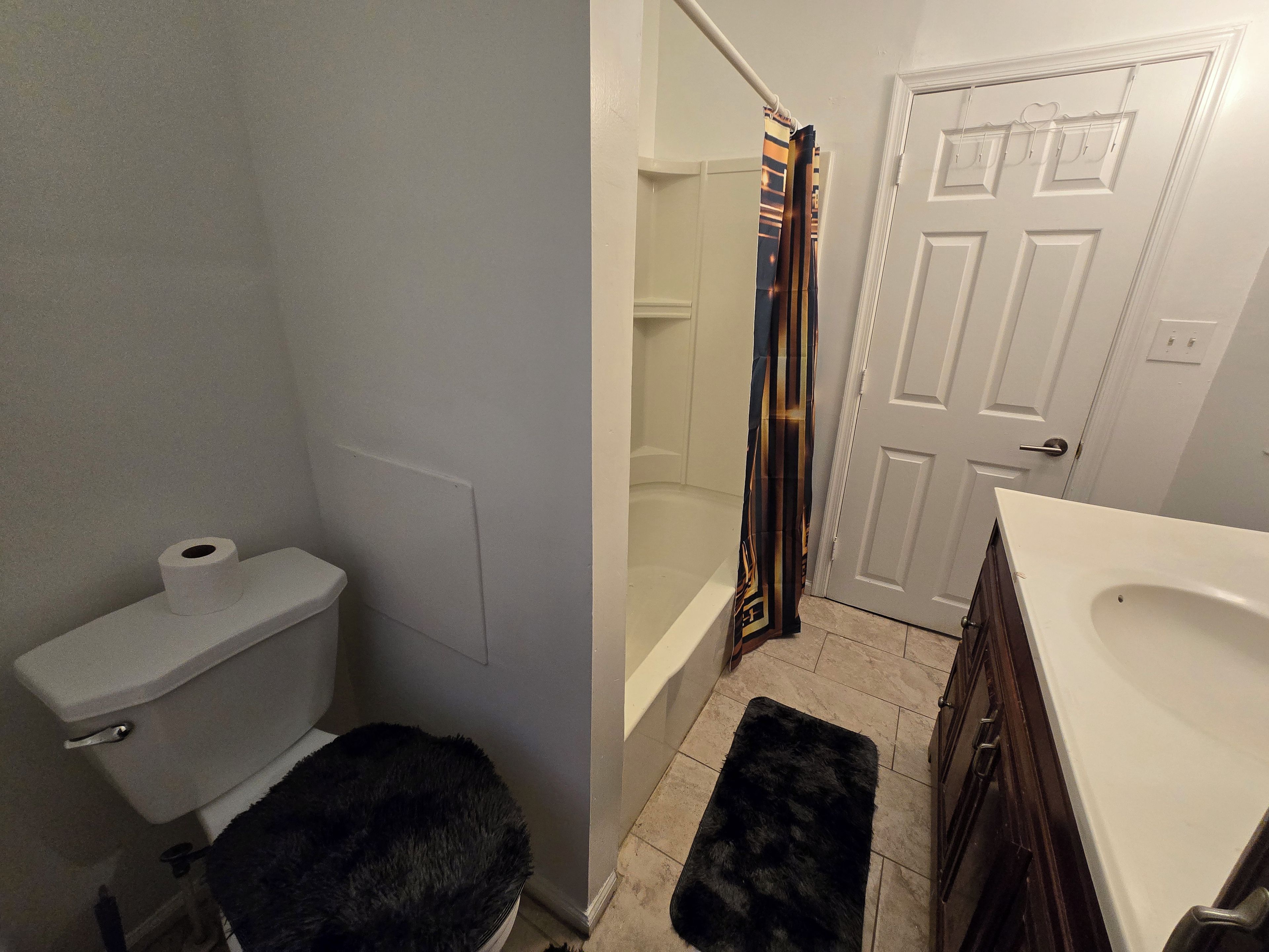 A bathroom with a toilet, a black rug, a bathtub, and a shower curtain.
