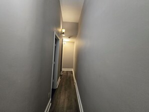 Un pasillo estrecho con piso de madera y molduras blancas, que conduce a una puerta al final.