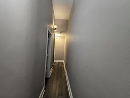 Un pasillo estrecho con piso de madera y molduras blancas, que conduce a una puerta al final.