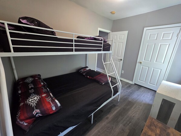 A bunk bed with a ladder, a door, and a small table in a room with grey walls and wooden flooring.