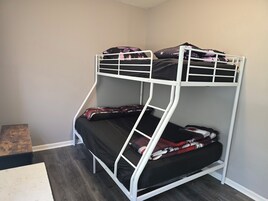 Una cama litera con estructura metálica blanca, ropa de cama negra y almohadas estampadas.