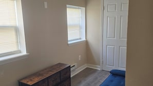 Una habitación con dos ventanas, una puerta, un banco y un sofá azul.