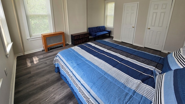 Un dormitorio con una cama grande, un banco, dos puertas y una ventana con persianas.