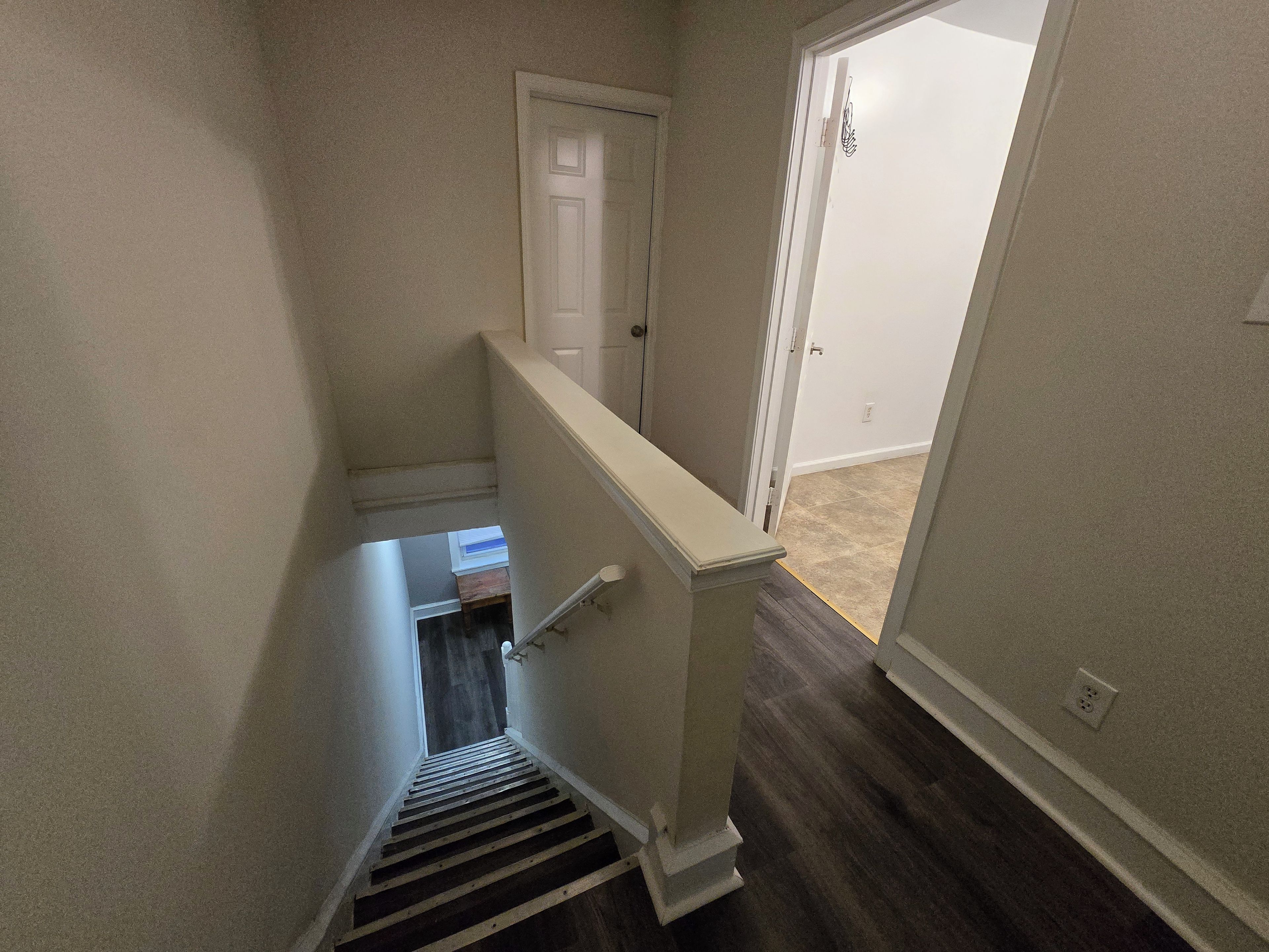 A narrow stairway with a handrail leading to a landing, a door at the top, and a carpeted floor.