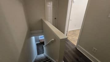 A narrow stairway with a handrail leading to a landing, a door at the top, and a carpeted floor.
