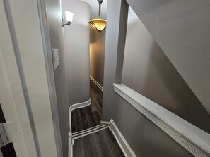 A narrow hallway with a wooden floor, a white baseboard, and a wall-mounted light fixture.