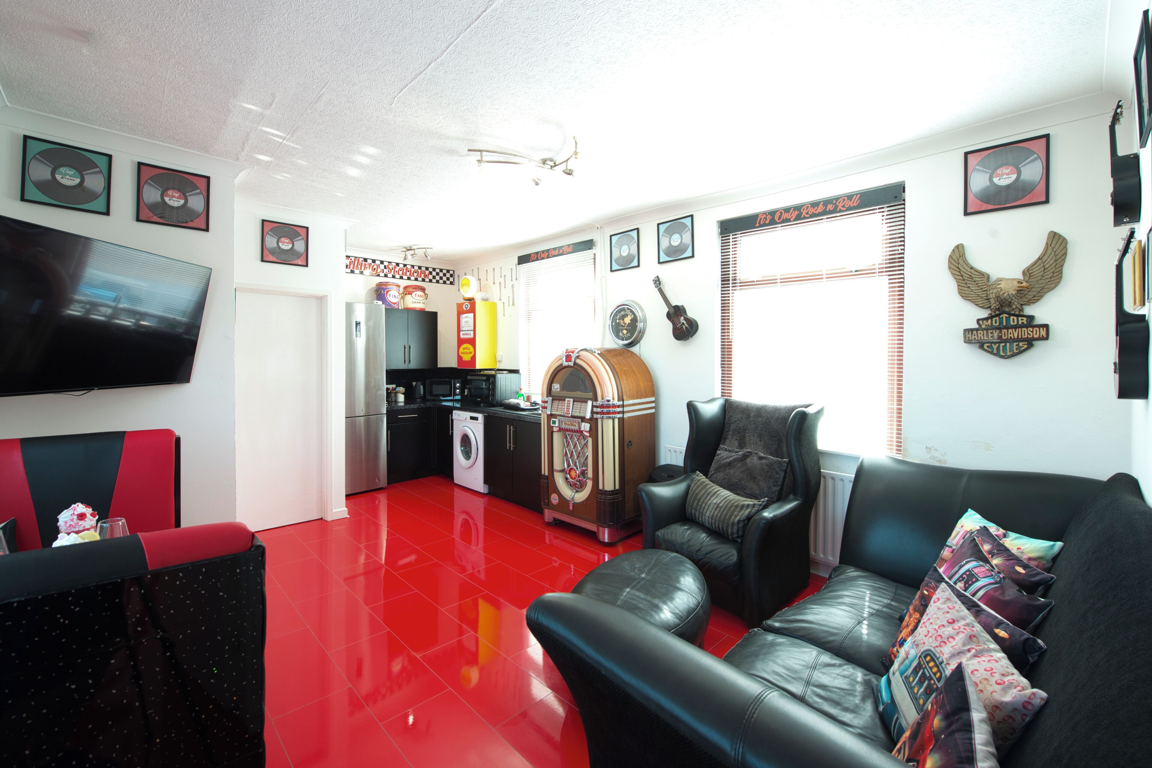 Una sala de estar con piso rojo, un sofá de cuero negro, un televisor de pantalla plana y un juke-box antiguo.