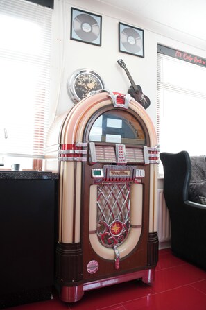 Ein Vintage-Jukebox mit Glastür, eine Gitarre und gerahmte Schallplatten an der Wand.
