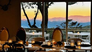 A dining area with tables set for two, candles, and a view of mountains through large windows. - Coca-Cola Cabin @Fire Mountain Estate & Club. Endless views, Fire Pit, Jacuzzi! (Scaly Mountain)