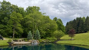 A tranquil pond with a waterfall, surrounded by lush greenery and trees. - Coca-Cola Cabin @Fire Mountain Estate & Club. Endless views, Fire Pit, Jacuzzi! (Scaly Mountain)
