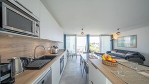 Et moderne køkken med indbygget mikroovn, kaffemaskine og vask. Der er et spiseområde med bord og stole, og en sofa i baggrunden.