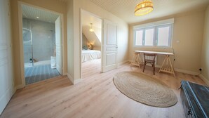 A spacious room with a wooden floor, a standing desk, a chair, a large window, and a ceiling light fixture. - Le Grand Large : Maison de Maître face mer (Penmarch)