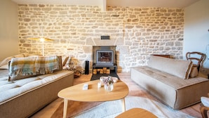 A cozy living room with a stone wall, a fireplace, a sofa, and a coffee table. - Le Grand Large : Maison de Maître face mer (Penmarch)