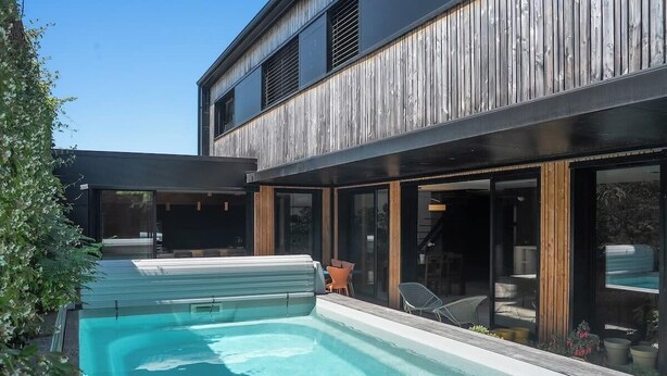 A modern house with a swimming pool, large windows, and a wooden exterior.