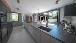 A modern kitchen with a large island, built-in appliances, and large windows offering views of the outdoors.