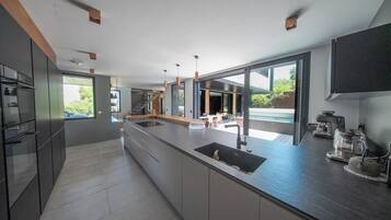 Een moderne keuken met een groot eiland, inbouwapparatuur en grote ramen met uitzicht op de omgeving.