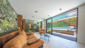A modern living room with a large sofa, a coffee table, and a view of a garden through large windows.