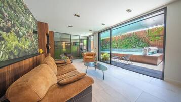 Een moderne woonkamer met een grote bank, een bijzettafeltje en uitzicht op een tuin door grote ramen.