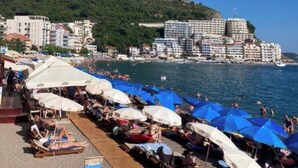 Un hotel costero con asientos frente a la playa, piscina y vistas al mar y edificios cercanos.