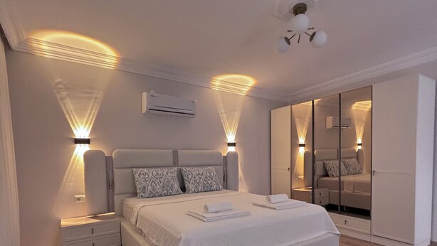 A bedroom with a bed, bedside tables, a wardrobe, and a ceiling light fixture. - Estelluzy Apart (Antalya)
