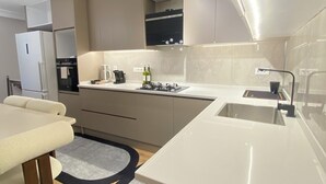 A modern kitchen with a built-in oven, a sink, and a dining area with a table and chairs. - Estelluzy Apart (Antalya)