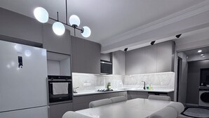 A modern kitchen with a built-in refrigerator, a dining table with cushioned chairs, and a pendant light fixture. - Estelluzy Apart (Antalya)