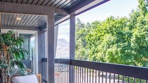 A balcony with wicker furniture, a round table, and a view of a parking area and greenery. - LUXURY DOWNTOWN WATERFRONT RETREAT with Park, Lake and Marina Views (Kelowna)