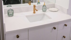 A bathroom with a white vanity, a large mirror, a gold faucet, and a glass soap dispenser. - LUXURY DOWNTOWN WATERFRONT RETREAT with Park, Lake and Marina Views (Kelowna)