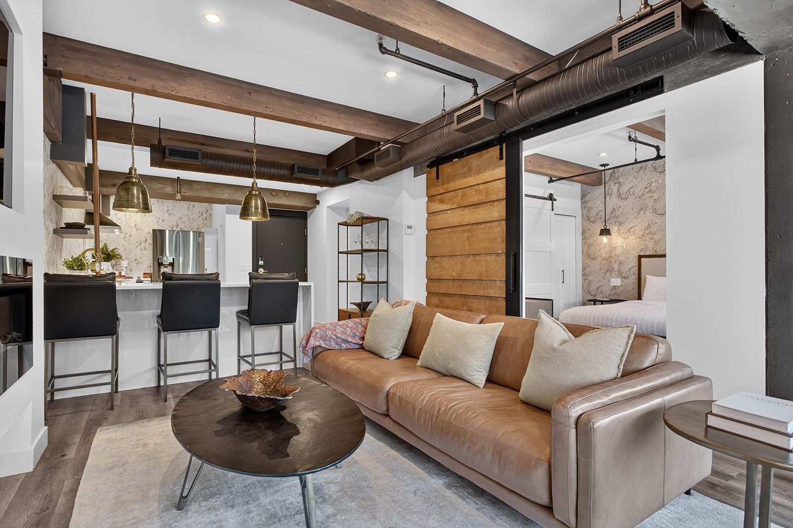 A modern living room with a leather sofa, a coffee table, and a kitchen area in the background.