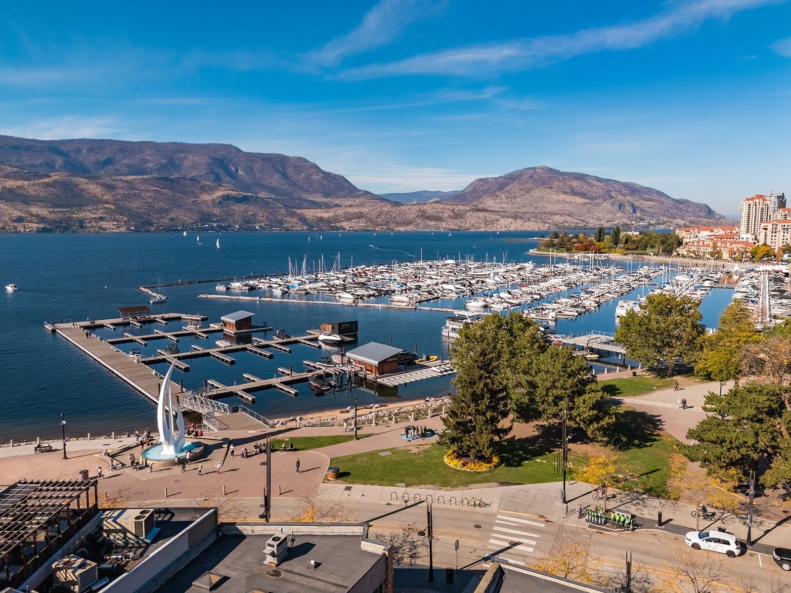 A marina with boats docked, a pedestrian walkway, and a view of the surrounding hills.
