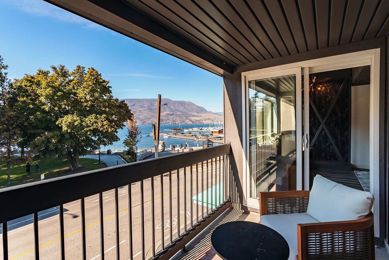 A balcony with a view of a marina and mountains, a wicker chair, and a table.