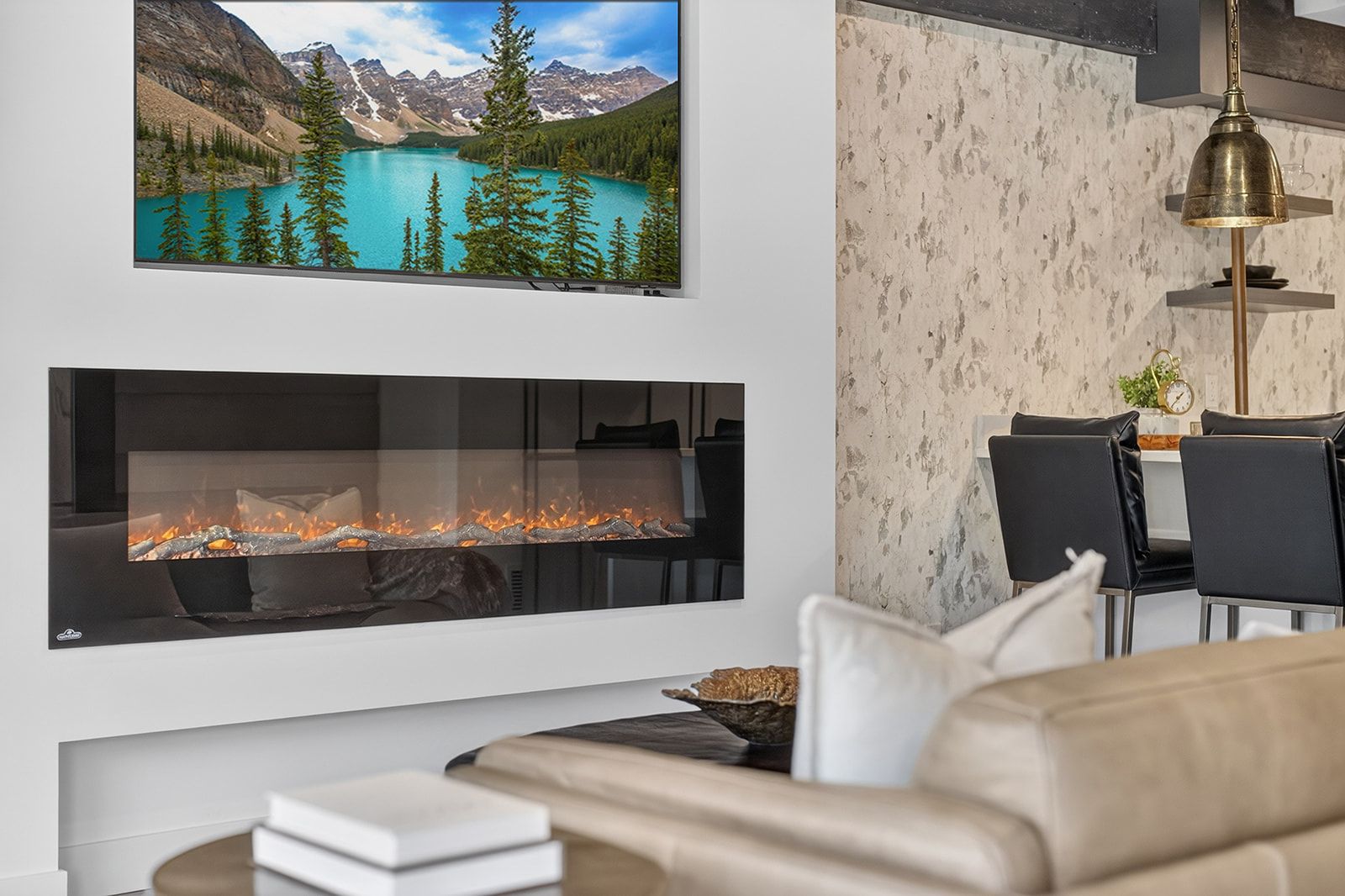 A modern living room with a fireplace, a mounted TV displaying a mountain landscape, and a dining area with chairs and a table.