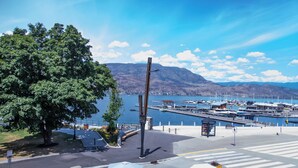 A marina with boats docked, a pedestrian crossing, and a clear view of the water and mountains in the background. - LUXURY DOWNTOWN WATERFRONT RETREAT with Park, Lake and Marina Views (Kelowna)