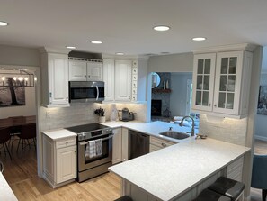 Una cocina moderna con armarios blancos, horno empotrado, microondas e isla grande con lavamanos.