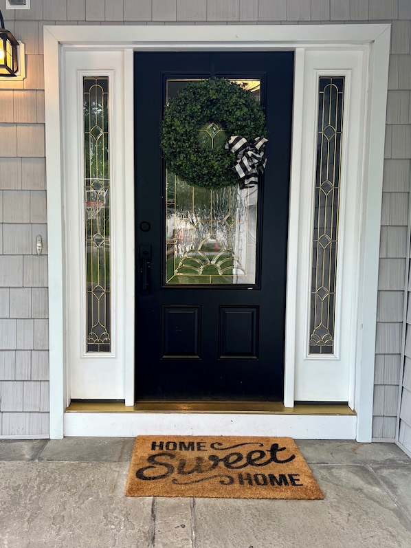 Una puerta principal oscura con paneles de vidrio decorativos, un adorno y un felpudo con el texto 'HOME Sweet HOME'.