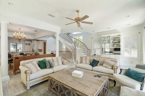 A spacious living room with a high ceiling, a chandelier, a ceiling fan, and a staircase leading to another level. - Ocean Manor - 4 Bikes, Shared Pool, Pet Friendly! (Destin)