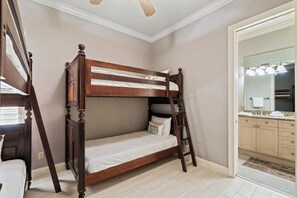 A bunk bed with a ladder, a bathroom with a mirror and sink, and a hallway with a ceiling fan. - Ocean Manor - 4 Bikes, Shared Pool, Pet Friendly! (Destin)