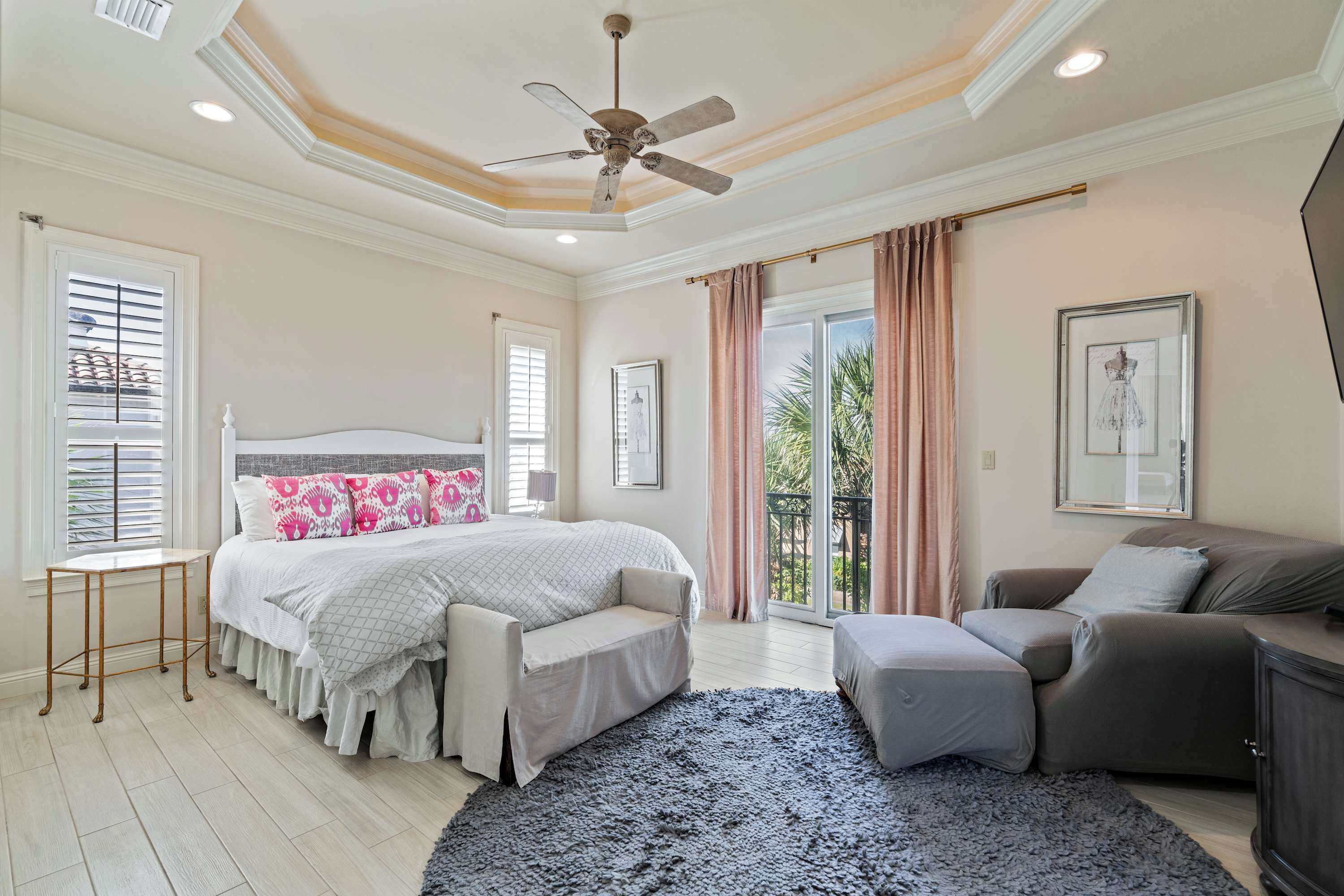 A bedroom with a bed, a sofa, a chair, a ceiling fan, and a large window.